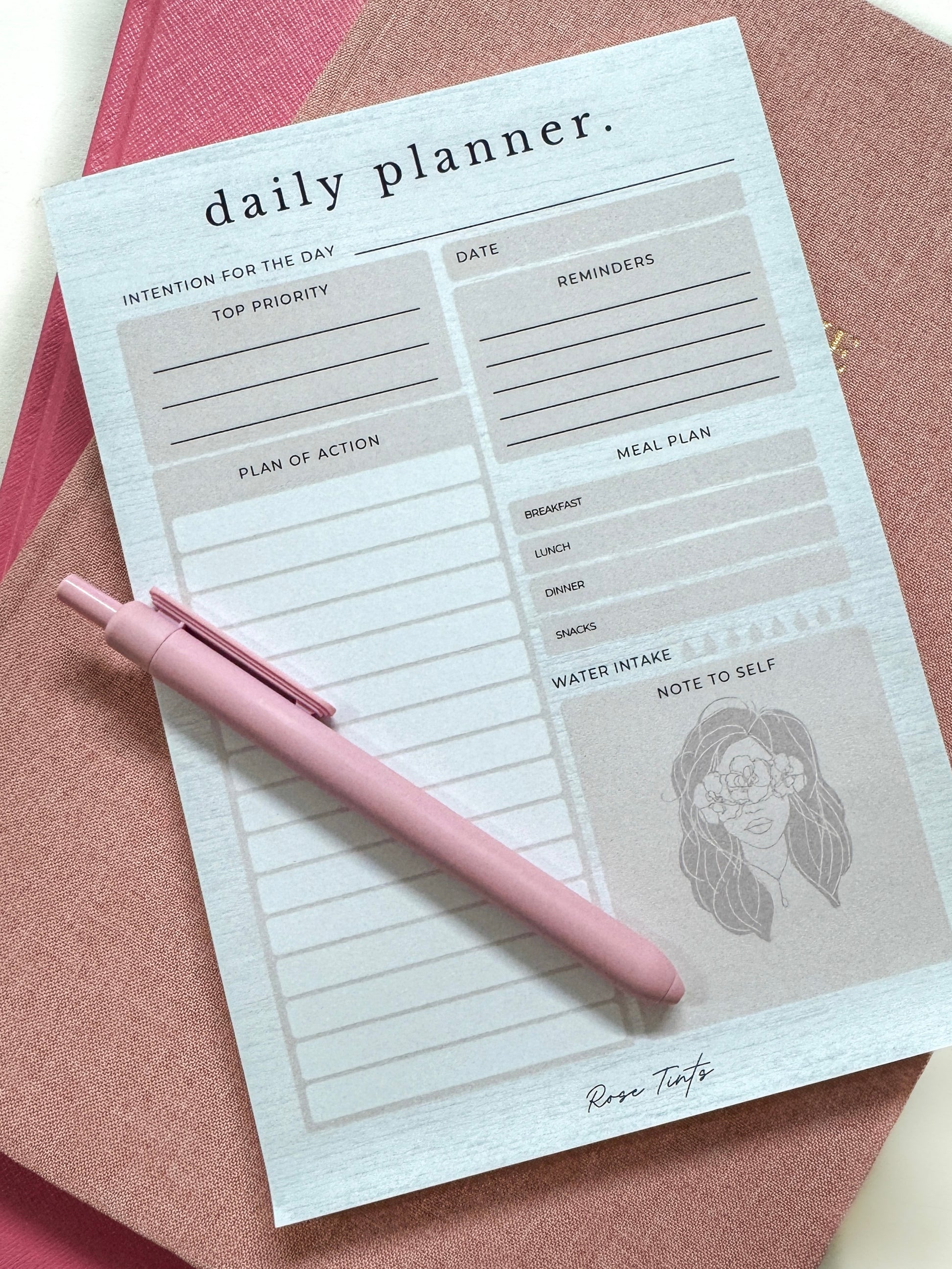 Daily planner with a pink pen on a pink surface