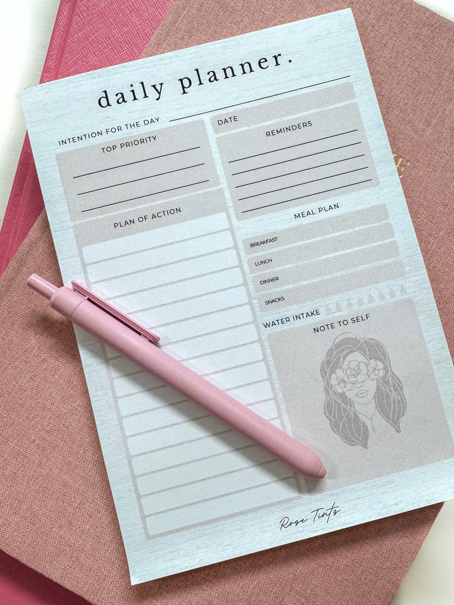 Daily planner with a pink pen on a pink surface